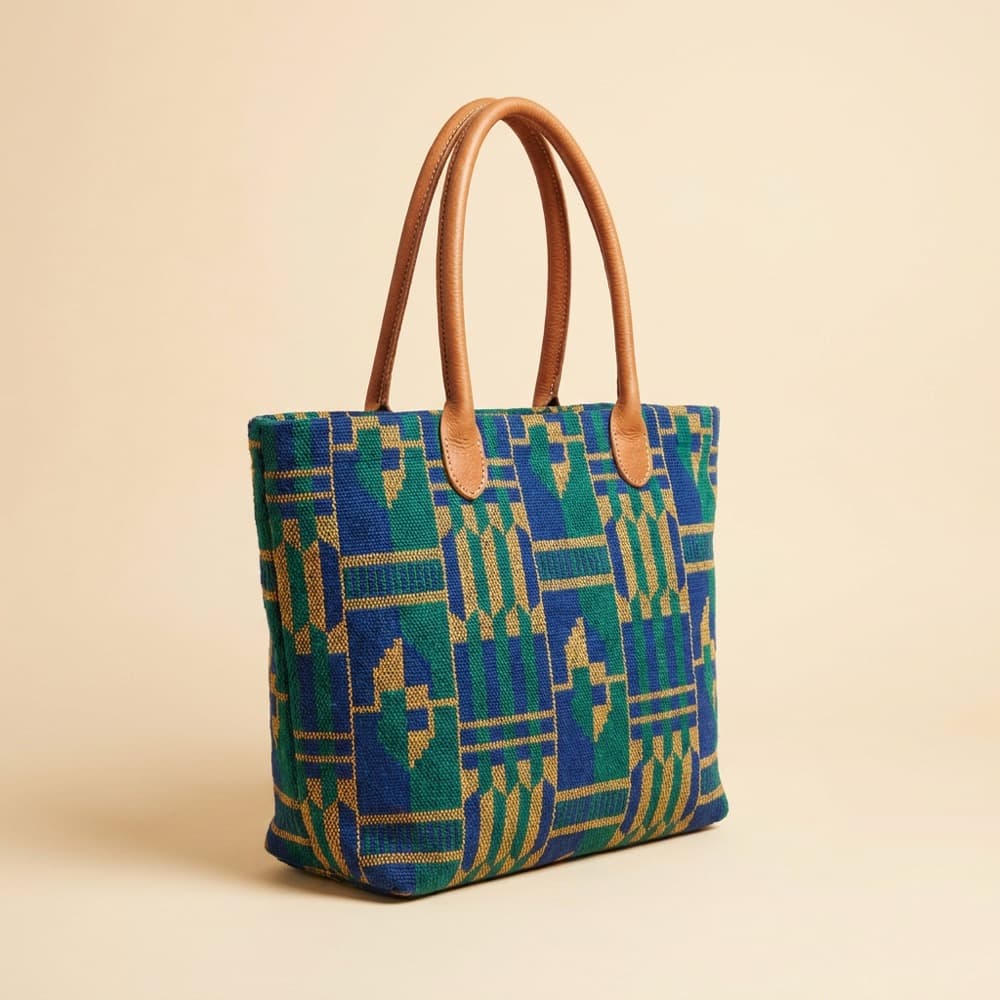 A woven kente patterned tote bag with leather handles on a plain background.